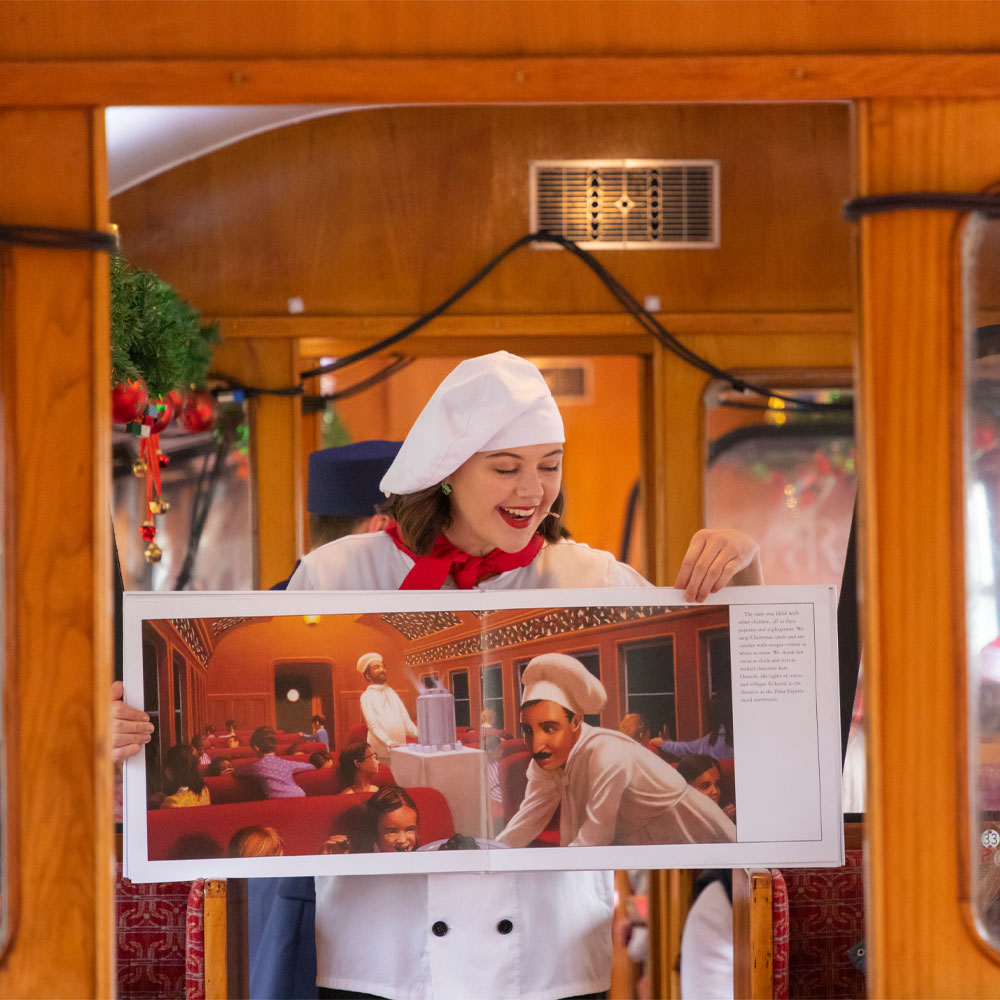 A chef on board The Polar Express Train Ride South Devon displaying The Polar Express book